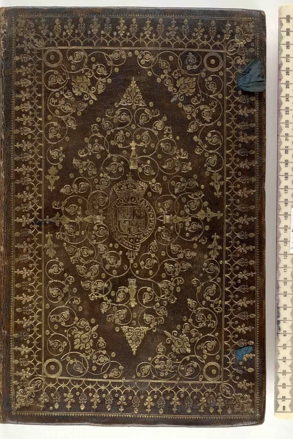 A worn old leather binding with rubbed corners and tooled decoration, beside a ruler