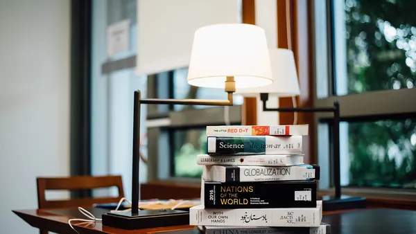 Stacks of books on a long table under reading lamps